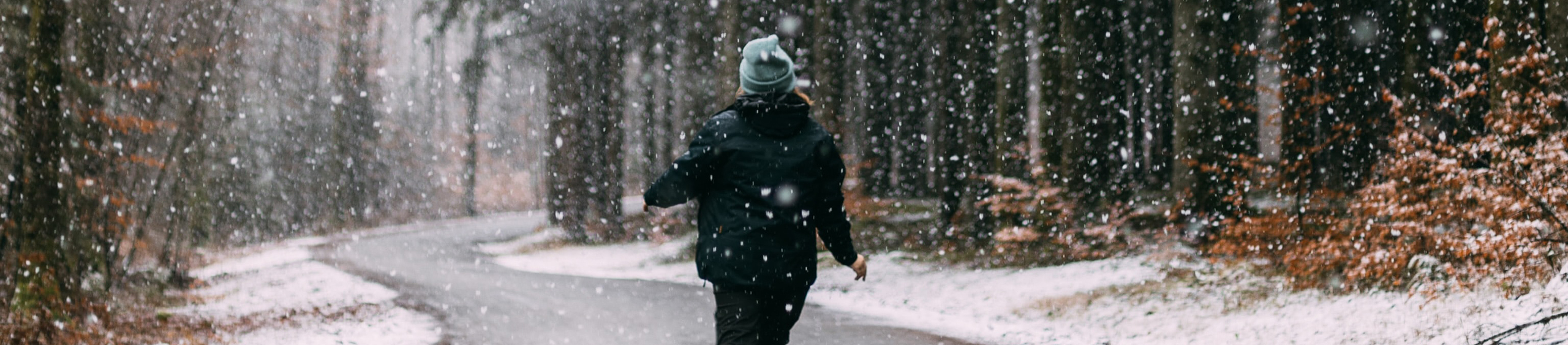 Woman walking on path in woods in the winter with snow falling down